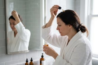 Femme appliquant un sérum anti-chute de cheveux sur son cuir chevelu devant un miroir de salle de bain